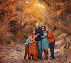 a family posing for a photo in the woods with fall foliage behind them and trees turning orange