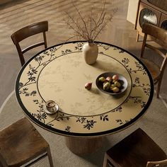 a bowl of fruit is sitting on a round table with chairs and a vase in the middle