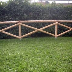 a wooden fence sitting on top of a lush green grass covered field next to a hedge