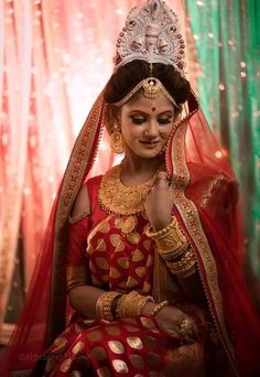 a woman wearing a red and gold bridal outfit sitting in front of a curtain