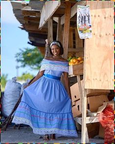 a woman in a blue dress standing next to a wooden stand with fruit on it