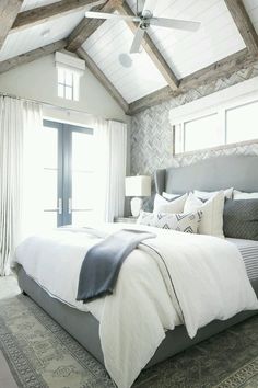 a large bed sitting under a ceiling fan in a bedroom next to a window with white curtains