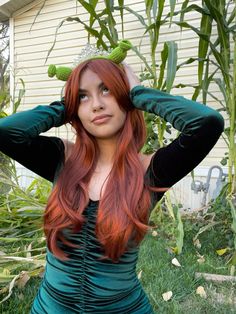 a woman with long red hair wearing a green dress and holding her hands on her head