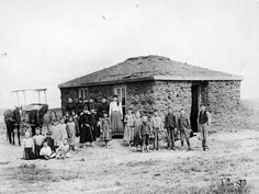 an old black and white photo of people standing in front of a small brick building