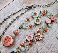 a close up of a necklace on a wooden surface with beads and flowers hanging from it