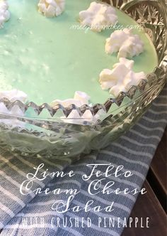 a green cake with marshmallows on top in a glass pie dish sitting on a blue and white checkered table cloth