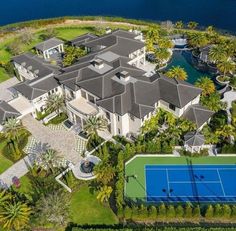 an aerial view of a mansion with a tennis court in the foreground and palm trees surrounding it