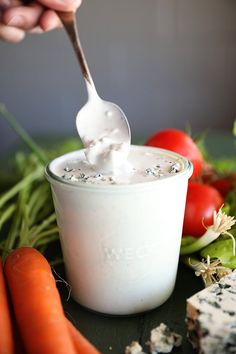 a person holding a spoon full of yogurt next to carrots and celery