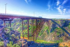 a large bridge spanning over a canyon with mountains in the background and blue skies above