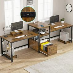 a computer desk with two computers on it and a clock above the desk, in front of a window