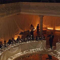 a group of people standing around tables in a room with white drapes on the ceiling