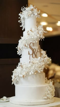 a three tiered wedding cake with white flowers on the top and initials on the bottom