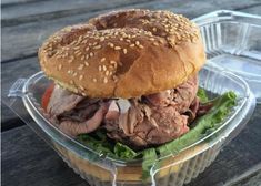 a sandwich with meat and lettuce in a plastic container on a wooden table