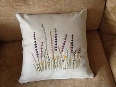 a white pillow with flowers on it sitting on a couch next to a brown chair