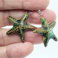 two green starfish shaped glass pendants in the shape of sea stars are being held by a person's hand