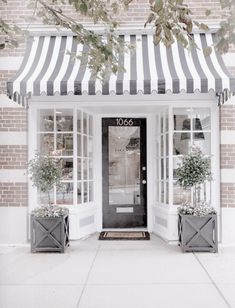 a black and white striped awning over a store front with potted plants outside