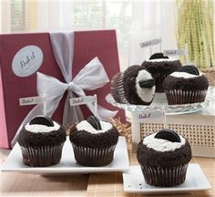 chocolate cupcakes with white frosting and black icing in front of a gift box