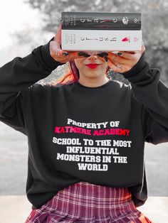 a woman holding up a book over her head with the words property of satane academy on it