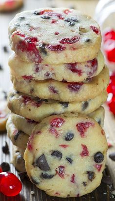 some cookies are stacked on top of each other with cherries and chocolate chips in the background