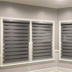 two windows with blinds in the corner of a room that has white trim on them