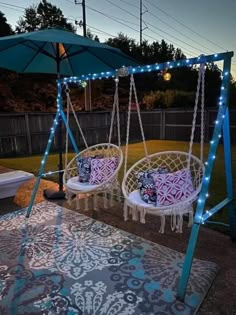 two hanging chairs with lights on them in front of a backyard patio table and umbrella