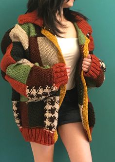 a woman standing in front of a blue wall wearing a multicolored knitted jacket