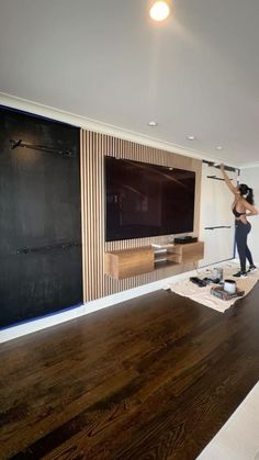 a woman standing in front of a flat screen tv mounted on a wall next to a wooden floor