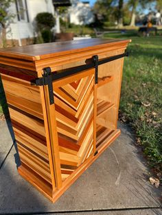 a wooden cabinet sitting on top of a sidewalk next to a grass covered park area