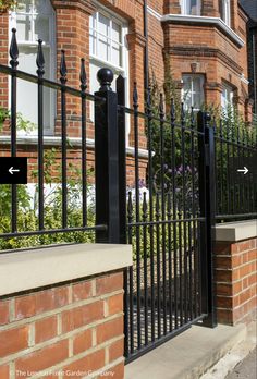 a brick building with black iron fence and flowers on the sidewalk in front of it