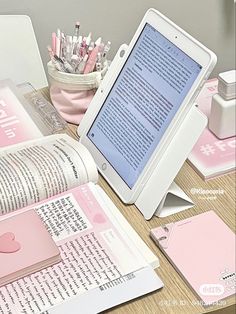 an open book sitting on top of a table next to a tablet computer and pen holder