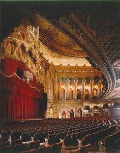 an empty theater with red curtains and seats in it's center aisle, looking toward the stage