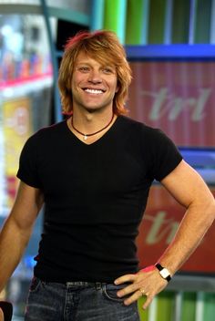 a man in black shirt standing with his hands on his hips and smiling at the camera