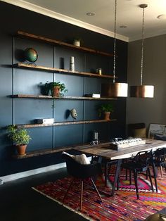 a dining room table with chairs and shelves on the wall behind it, along with potted plants