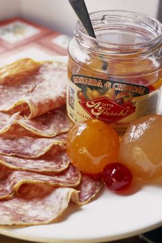 a plate topped with ham and jelly next to a jar of jam on a table