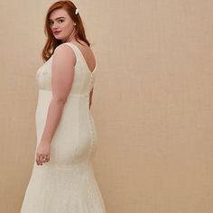 a woman in a white wedding dress standing up against a beige wall with her hands on her hips