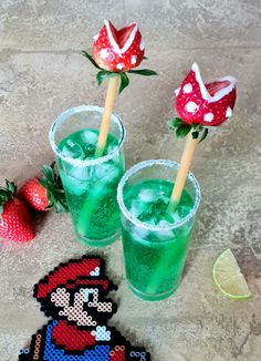 two glasses filled with green liquid next to strawberries and an ornament on the table