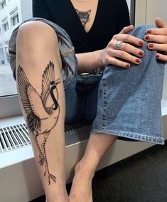 a woman sitting on a window sill with a bird tattoo on her arm and leg