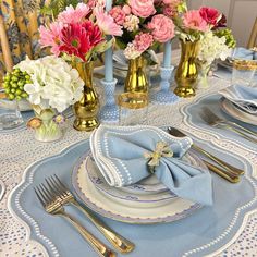 the table is set with blue and white plates, silverware, and pink flowers