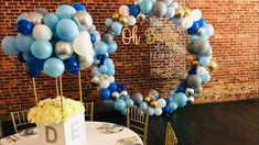 a table topped with blue, white and gold balloons in front of a brick wall