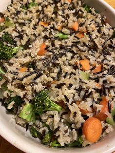 a white bowl filled with rice, carrots and broccoli on top of a wooden table