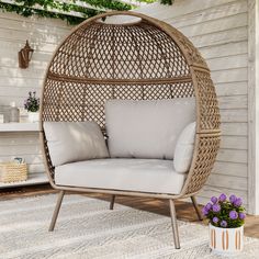 a wicker hanging chair with white cushions on a patio floor next to a potted plant