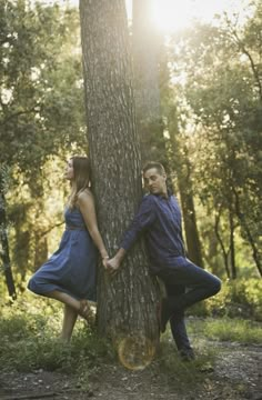 a man and woman leaning against a tree in the woods