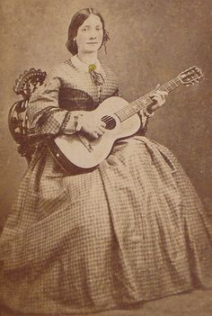 an old time photo of a woman in a dress holding a guitar and posing for the camera