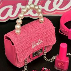 a pink purse with pearls on the handle and chain attached to it, sitting next to other accessories