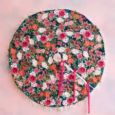 a clock made out of fabric with flowers and fringes on the face, sitting in front of a pink wall