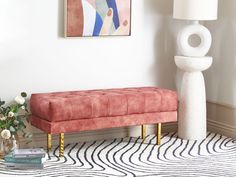 a pink bench sitting next to a white vase on top of a rug in a living room