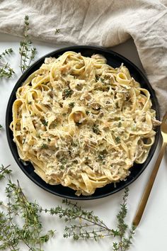 a black plate topped with pasta covered in sauce and herbs next to a gold spoon