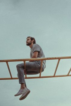 a man is sitting on the edge of a metal beam and looking up at the sky