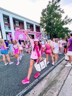 a group of women in pink and blue outfits walking down the street with their arms up