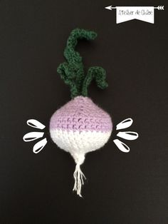 a crocheted radish on a black surface with white flowers and green stems